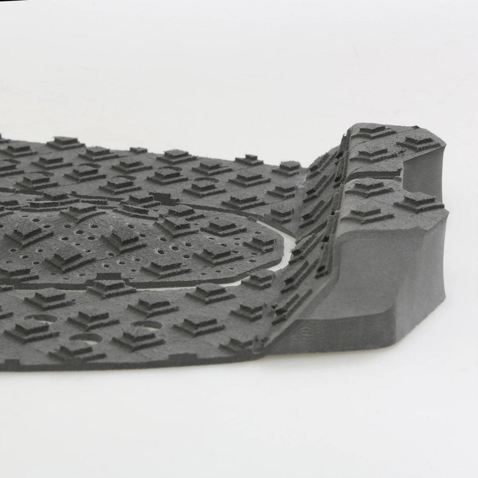 Eine Nahaufnahme einer grauen Gummifußmatte mit erhabenen, kantigen Profilen und einer erhöhten Kante, ähnlich dem strukturierten Griff des FCS T-3 Eco Eclipse Tailpad von FCS.