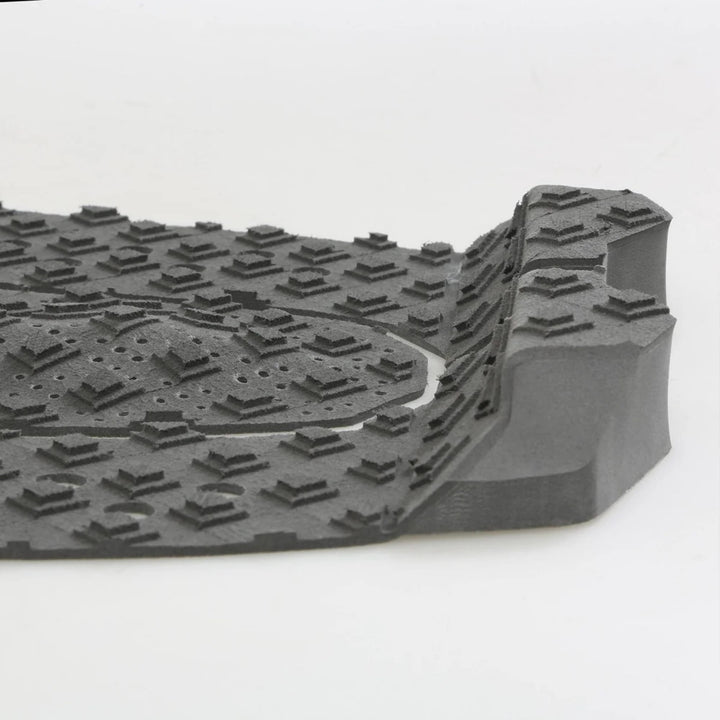 Eine Nahaufnahme einer grauen Gummifußmatte mit erhabenen, kantigen Profilen und einer erhöhten Kante, ähnlich dem strukturierten Griff des FCS T-3 Eco Eclipse Tailpad von FCS.