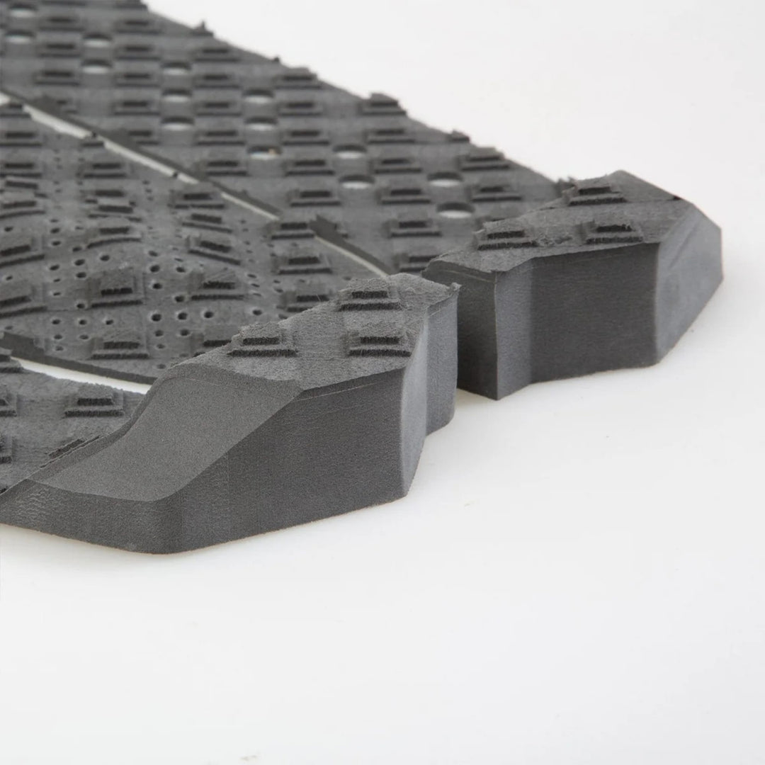 Nahaufnahme des FCS T-3 Eco Eclipse Tailpad von FCS, ein schwarzes, strukturiertes Surfboard-Tailpad aus Zuckerrohrschaum mit erhabenen Mustern und abgewinkelten Kanten für verbesserte Griffigkeit und Haltbarkeit.