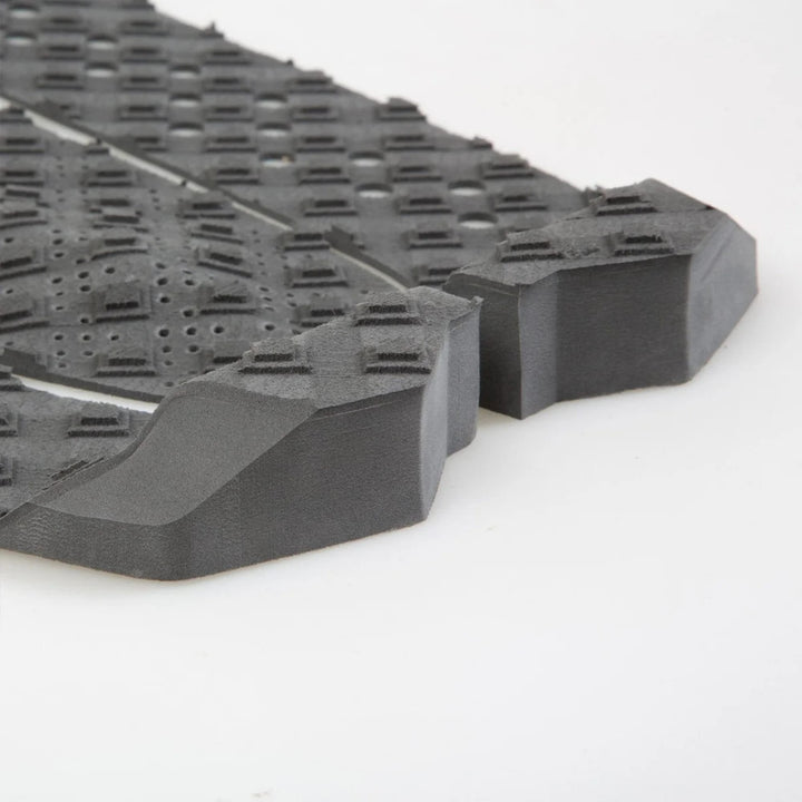 Nahaufnahme des FCS T-3 Eco Eclipse Tailpad von FCS, ein schwarzes, strukturiertes Surfboard-Tailpad aus Zuckerrohrschaum mit erhabenen Mustern und abgewinkelten Kanten für verbesserte Griffigkeit und Haltbarkeit.