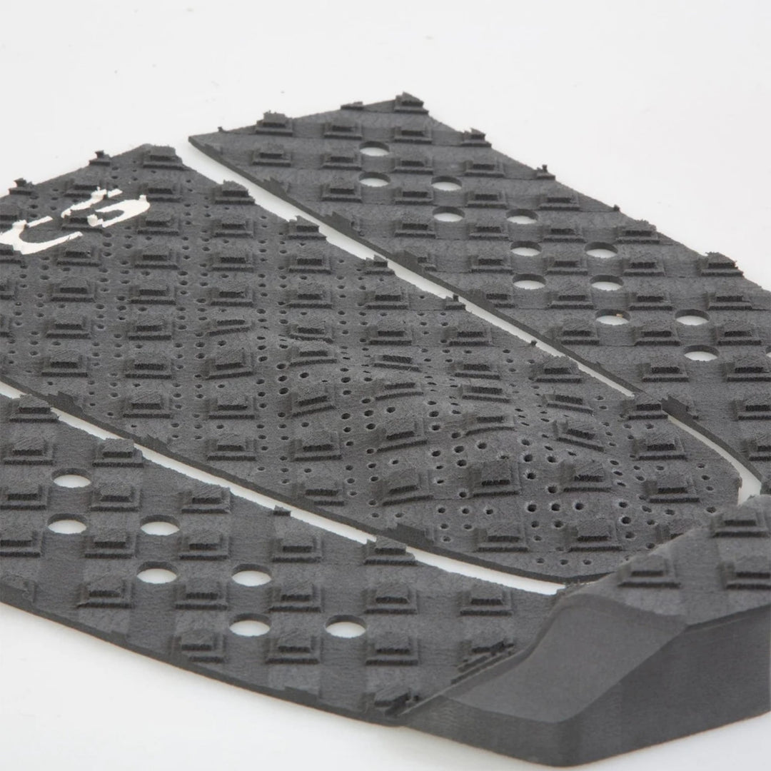 Eine Nahaufnahme des FCS T-3 Eco Eclipse Tailpads, ein schwarzes, strukturiertes Surfboard-Tailpad von FCS mit erhabenen Erhebungen und Löchern für den Grip, dargestellt vor einem schlichten weißen Hintergrund.