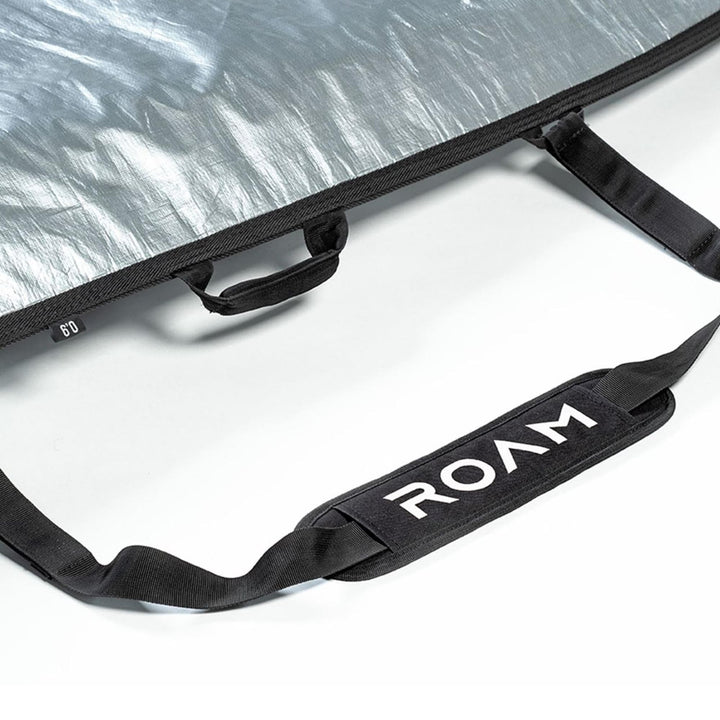 Eine Nahaufnahme eines schwarzen Griffs mit weißem ROAM-Branding auf einer strukturierten silbernen Roam Boardbag Surfboard Daylight Hybrid Fish, wobei auch zusätzliche schwarze Riemen sichtbar sind.