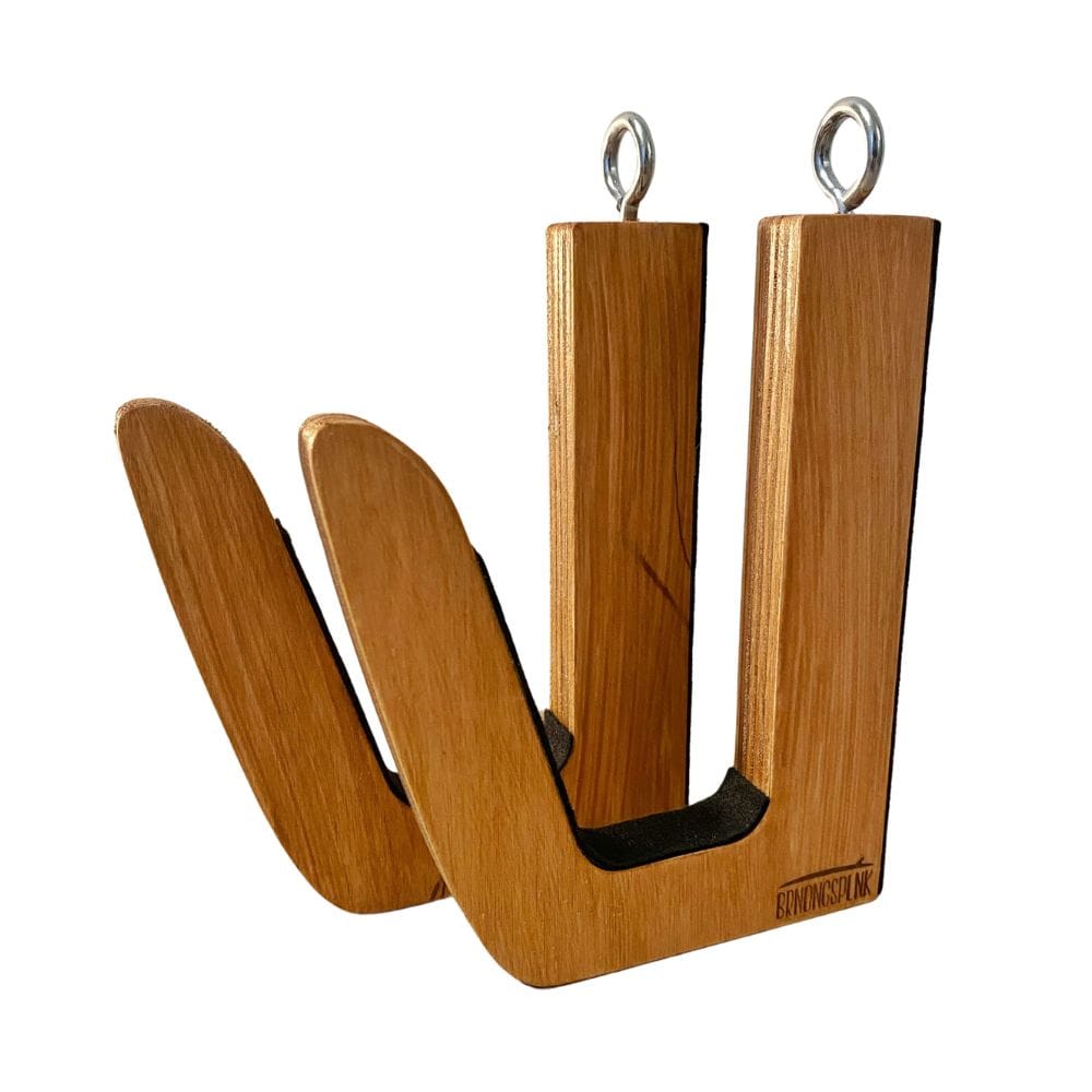 Die Surfboard Wandhalterung aus Holz von Brandungsplanke ist eine hellbraune, handgefertigte Holzhalterung mit zwei vertikalen Armen, Metallschlaufen an der Oberseite und schwarzer Polsterung im Inneren der Arme.