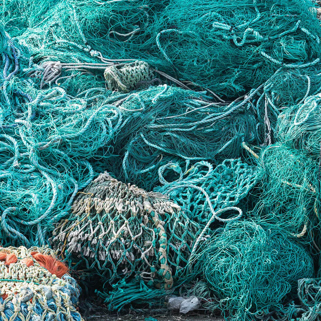 A Rebel Fin - Wachskamm von Sex Wax, hergestellt aus recycelten grünen und blauen Fischernetzen mit braunen und orangen Akzenten, wird im Freien in einem verhedderten Haufen gezeigt.