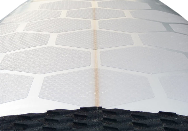 Nahaufnahme eines Riversurfboard-Decks mit RSPro - HexaTraction Pads (Riversurfboard Kit / 10 Stück) in Weiß, einem schwarzen Surfboard-Griff am unteren Rand und einer schwachen braunen Stringerlinie, die in der Mitte verläuft.
