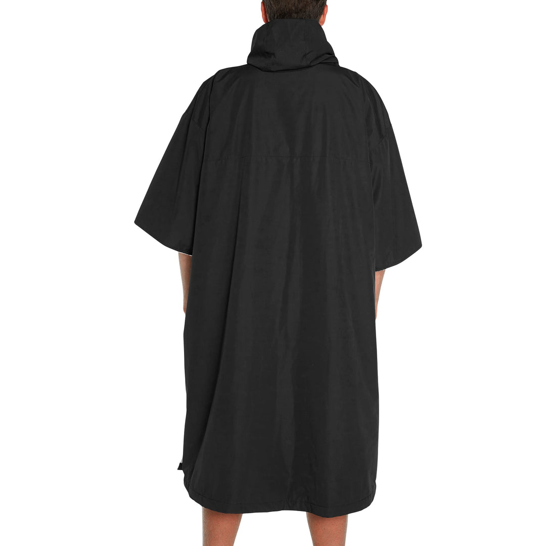 Eine Person schaut von der Kamera weg und trägt den FCS All Weather Surf Poncho (wasserfest) von FCS. Der locker sitzende, knielange Poncho mit weiten Ärmeln und Kapuze bedeckt den Großteil des Körpers, die Arme liegen entspannt an den Seiten.