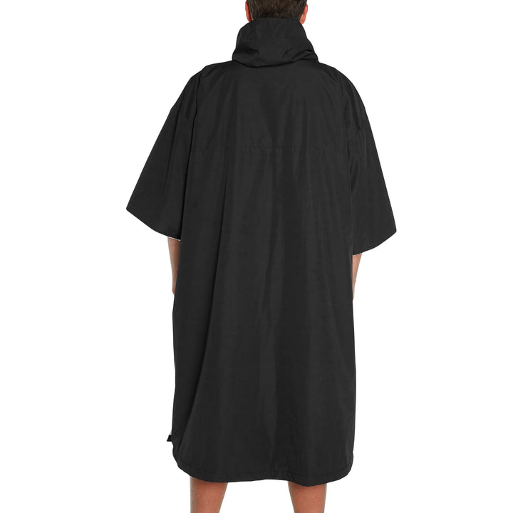 Eine Person schaut von der Kamera weg und trägt den FCS All Weather Surf Poncho (wasserfest) von FCS. Der locker sitzende, knielange Poncho mit weiten Ärmeln und Kapuze bedeckt den Großteil des Körpers, die Arme liegen entspannt an den Seiten.