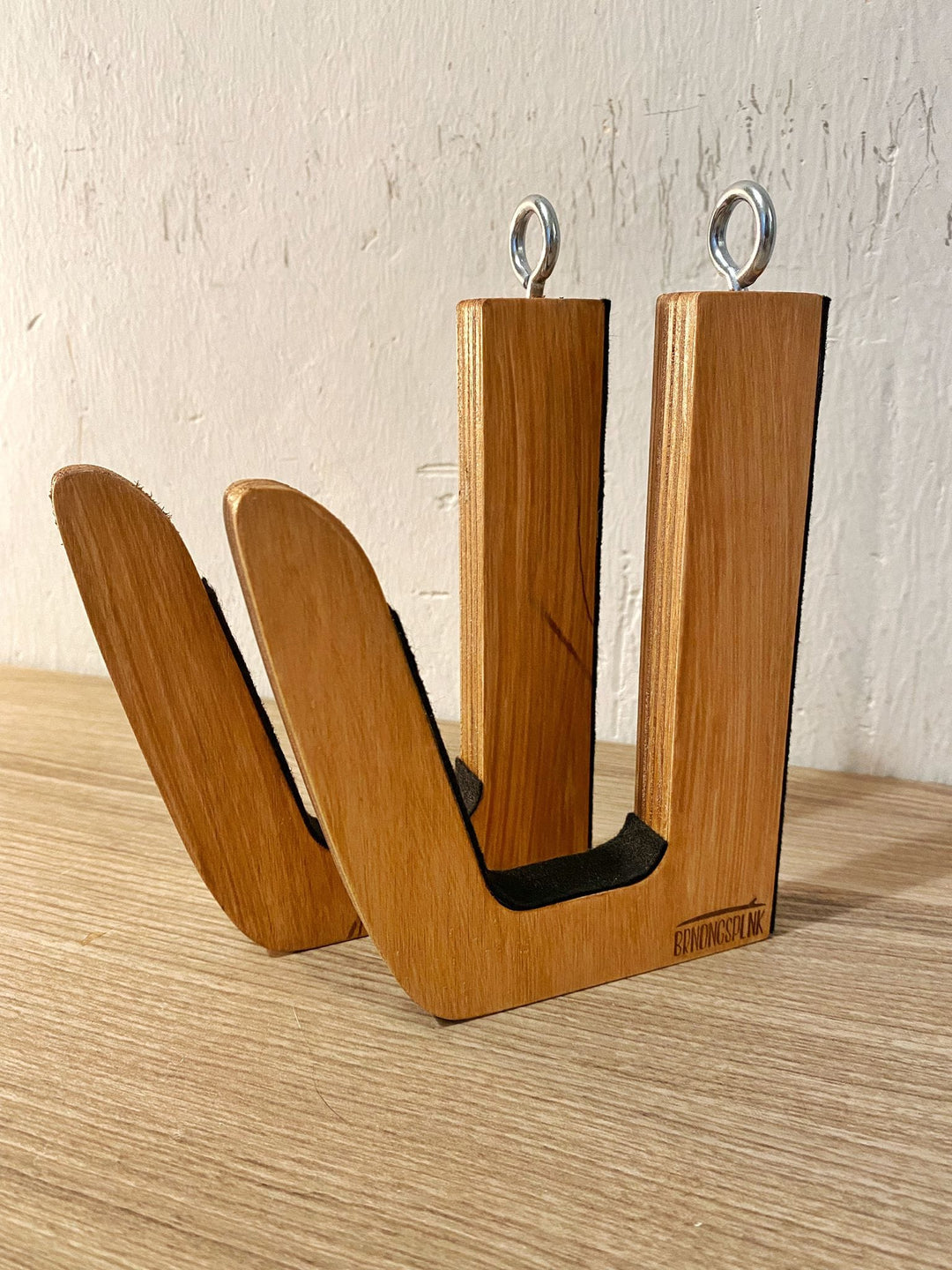 Die Brandungsplanke Surfboard Wandhalterung aus Holz verfügt über handgefertigte Holzhaken mit Metallösen und schwarzem Filzpolster - eine moderne, minimalistische Halterung, die sich perfekt für die Befestigung Ihres Boards an einer weißen Wand oder Holzoberfläche eignet.